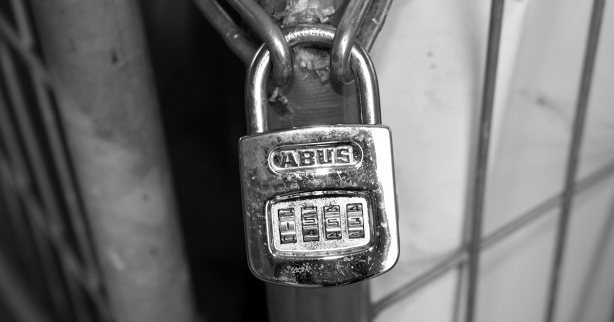 A greyscale close-up of a silver combination padlock attached to a metal gate.