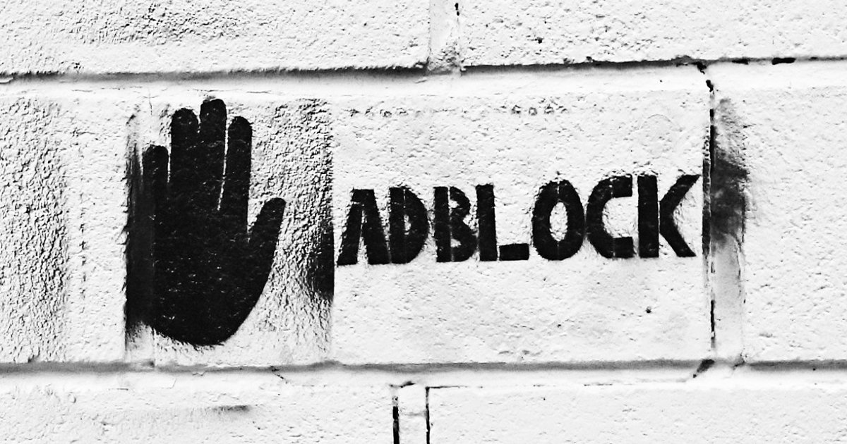 A black handprint and the word 'ADBLOCK' stencilled onto a white brick wall.